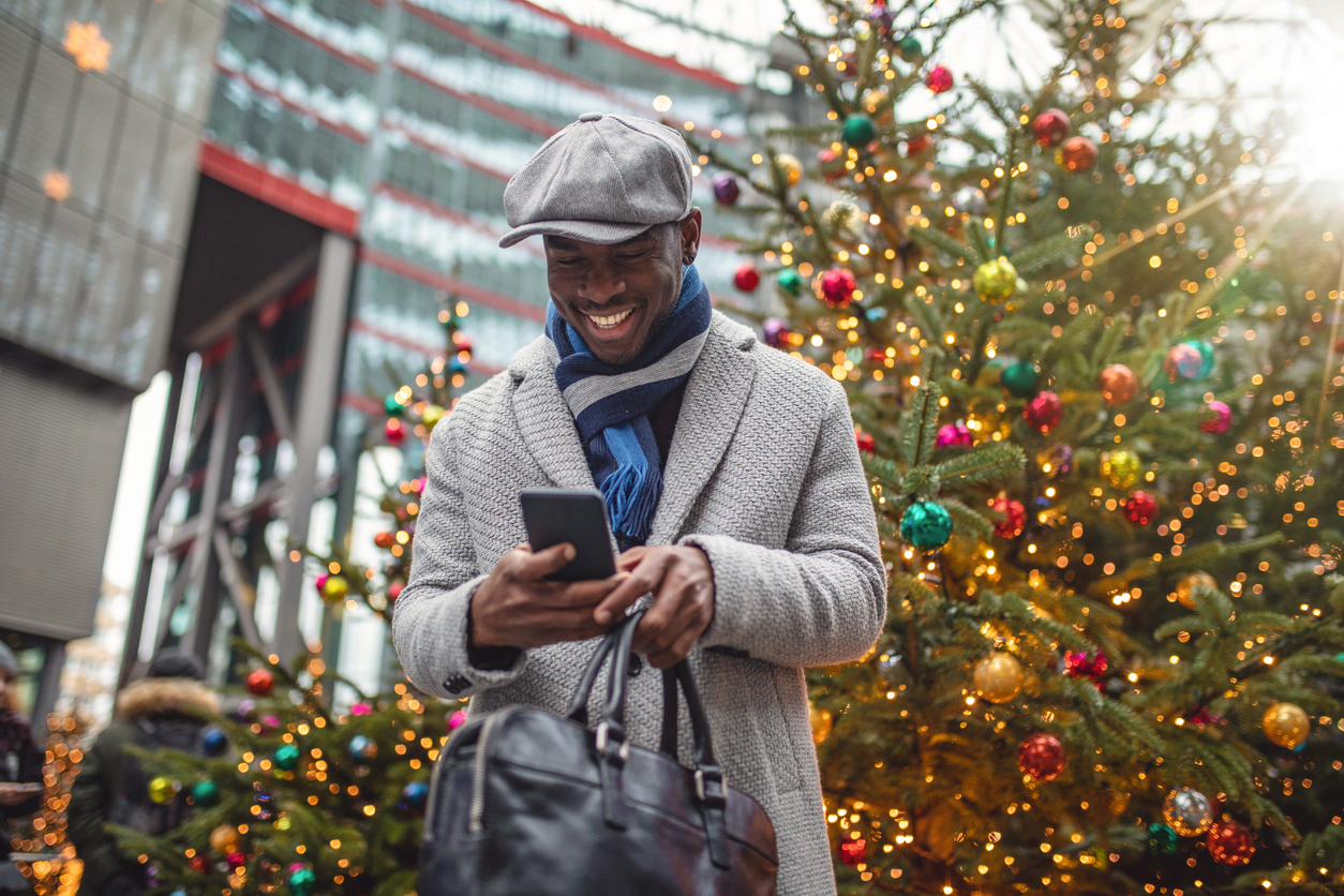 man-checking-phone-standing-by-christmas-trees-on-street