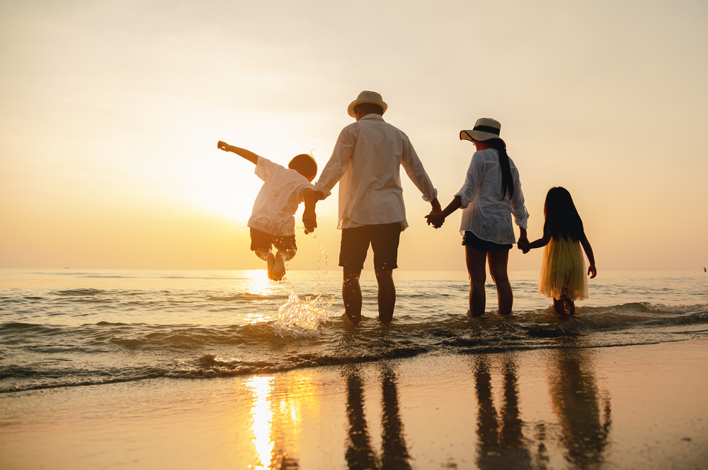 Generational Wealth - Happy family jumping together on the beach in holiday.